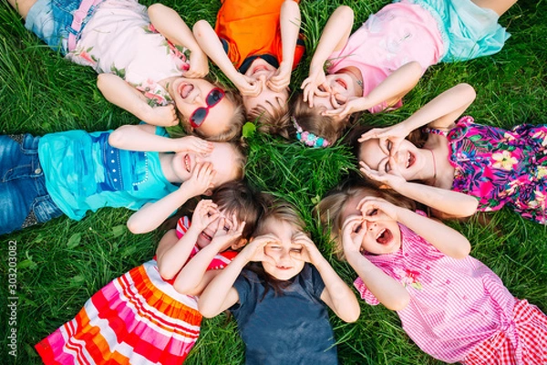 Fototapeta A group of children lying on the green grass in the Park. The interaction of the children.