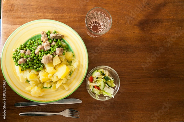 Fototapeta A dinner plate with peas, meat and potatoes with salad and a glass of water