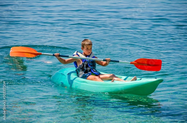 Obraz kayaking lessons. Boy with  life buoy suit in kayak lessons during summer vacations in an island of Greece.