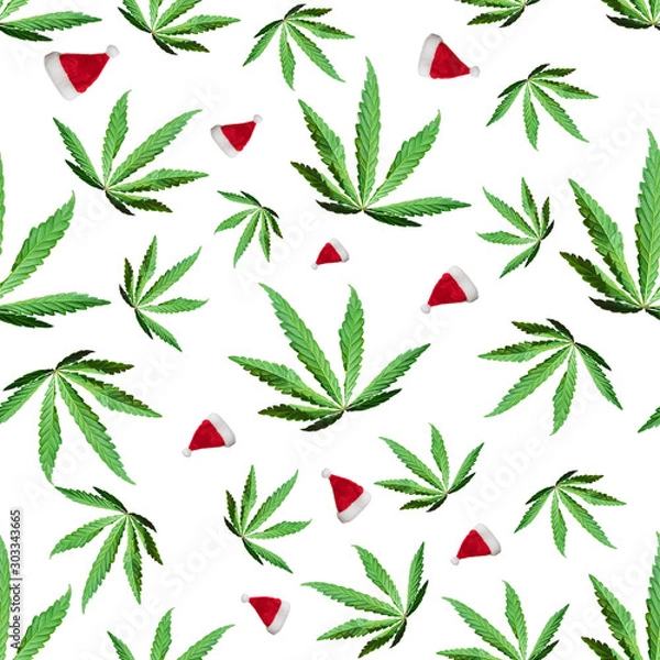 Fototapeta Green cannabis leaves and Santa Claus caps isolated on white background. Seamless texture. Top view, image Wallpaper close-up