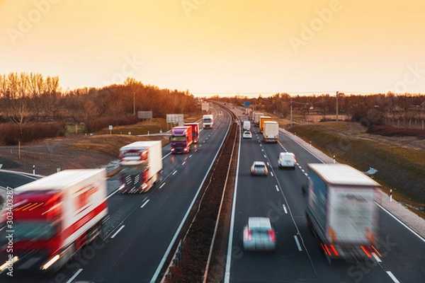 Fototapeta Ruchliwa autostrada z szybko poruszającymi się pojazdami w pięknym zachodzie słońca