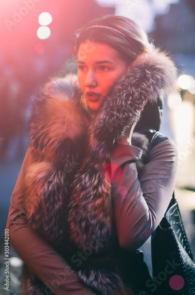 Obraz Beautiful caucasian girl  in winter clothes on the street, she looks in from top her  with a confident pose, she's in darkness illuminated by street and traffic lights