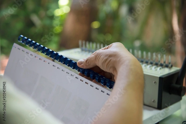 Obraz Man making report using comb binding machine - people working with stationary tools concept