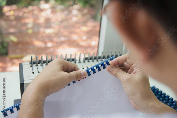 Obraz Man making report using comb binding machine - people working with stationary tools concept