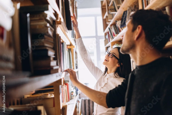 Obraz people, knowledge, education and school concept - happy student girl and the guy choose books in the old library