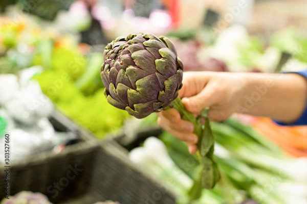 Fototapeta Woman's hand choosing artichoke in the market. Concept of healthy food, bio, vegetarian, diet.