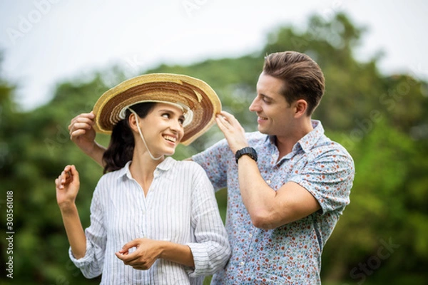 Fototapeta Outdoor shot of young couple in love joyful in the park through grass field. Man and woman hugging and  Laugh on grass field.