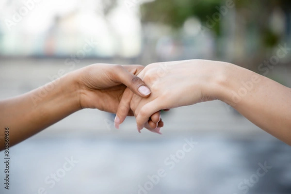 Fototapeta caucasian woman and african woman hand in hand, hand shaking to each other; concept of skin color tolerance, world peace, ethnicity understanding, team or teamwork