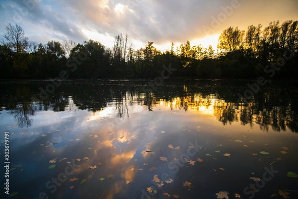 Obraz Sunset behind a small lake with pretty reflections and autumn leaves in the water