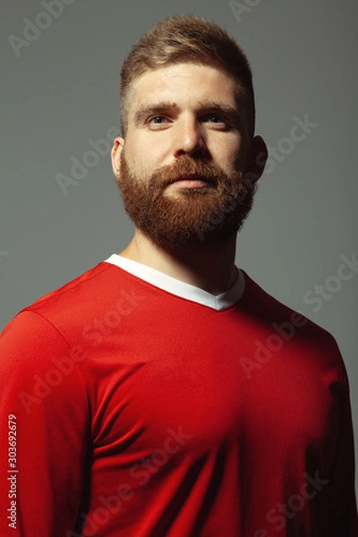 Fototapeta Middle aged handsome red-haired sport man over gray wall feeling proud of new sporting achievmen and enjoying the moment. Red sportswear. Football player. Hipster style. Vertical shot