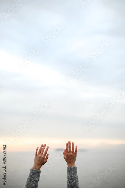 Fototapeta beautiful young hands in a warm woolen sweater raised up to the sky on a sunset background