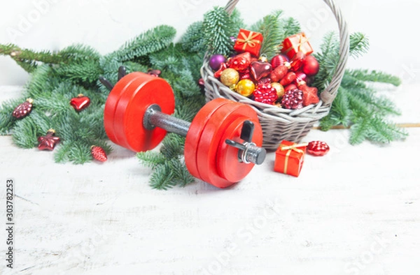 Obraz Christmas or New Year on a white background. Composition with dumbbells, gift, red glass balls, fir tree branches for healthy lifestyle and sport