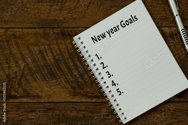 Fototapeta Table top view aerial image of 2020 new year business  goals & plans concept.Flat lay of essential object on brown wood.Text on notepad with black coffee and pen for accessories office desk backdrop