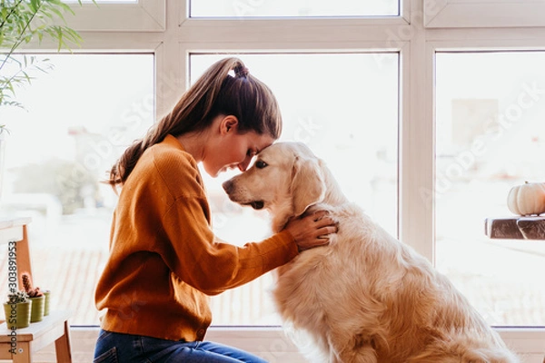 Obraz Zamknij piękną kobietę przytulającą swojego uroczego psa Golden Retriever w domu. Miłość do zwierząt koncepcja. Styl życia w pomieszczeniu