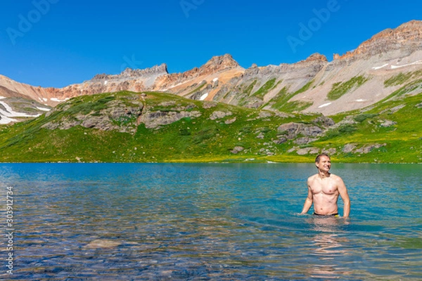 Fototapeta Young happy fit man standing swimming in cold colorful water of Ice Lake on famous trail in Silverton, Colorado in San Juan Mountains in summer