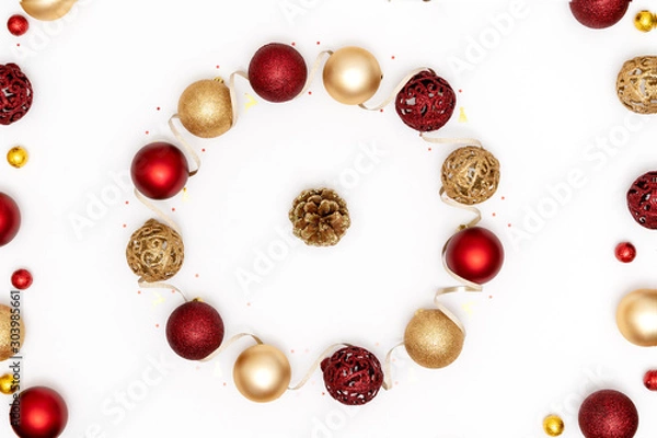 Fototapeta New Year and Christmas greeting card. Wreath made of red and golden Christmas decorations - shiny balls, pine cone and decorative ribbon on white paper background. Top view, flat lay, copy space