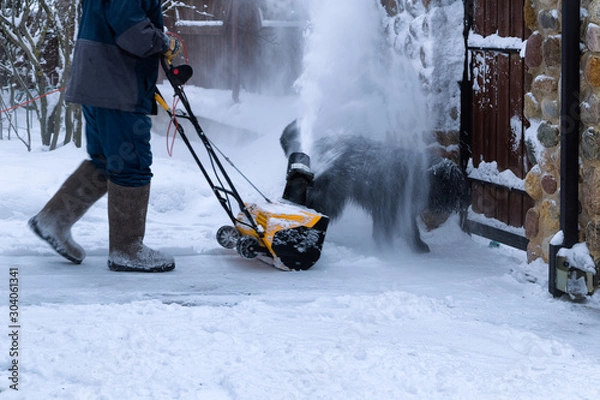 Fototapeta Man clears snow with a snow blower  in house yard. Snowblower in working. Snowy winter yard.