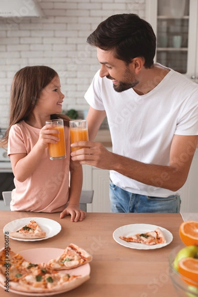 Fototapeta father clicking glasses with orange juice with daughter in the kitchen