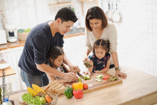 Fototapeta Young Asian love family are preparing the breakfast, sandwich vegetable on table in the kitchen which Excited smiling and felling happy. parent teach daughter to cooking food on the day at home.