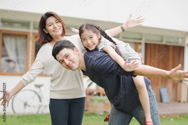 Fototapeta Young Asian family love, father mother and daughter standing playing and fun at outdoor in front of home. girl and parent looking at camera which smiling and felling happy. background is white house.