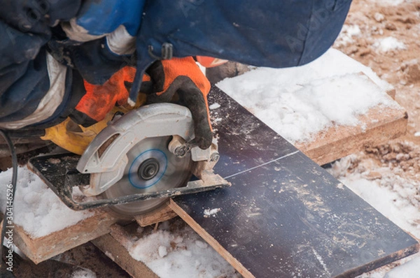 Fototapeta A worker cuts off part of a laminated board with a circular saw.
