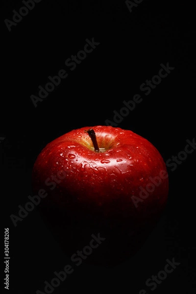 Fototapeta Appetizing red apple covered with drops of water on a black background. Close-up