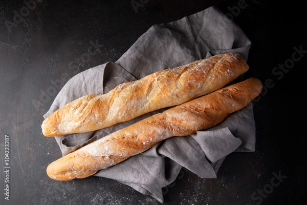 Fototapeta Fresh hot two baguettes on dark background. Top view.