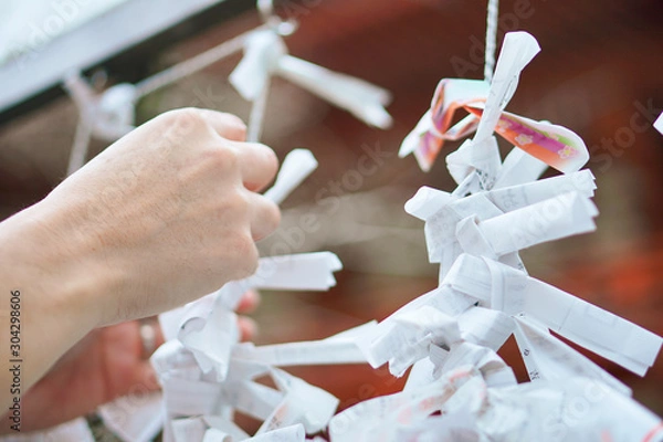 Obraz おみくじを神社の結びどころに結ぶ手。願い。神社に参拝、初詣、今年の運気。運勢を占う。