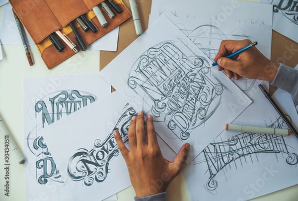 Fototapeta Typography Calligraphy artist designer drawing sketch writes letting spelled pen brush ink paper table artwork.Workplace design studio.