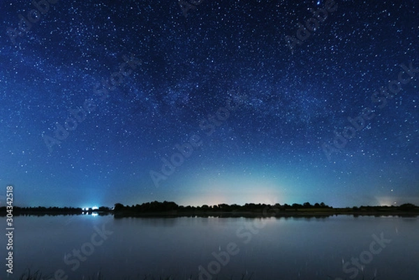 Fototapeta Magiczna gwiaździsta noc nad brzegiem rzeki z dużym drzewem i drogą mleczną na niebie i spadającymi gwiazdami latem.