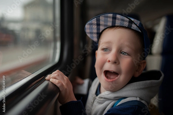 Fototapeta emotional boy in a blue cap and a gray jacket in a transport by the window