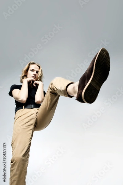 Obraz A young man with long blond hair  stepping on something, steps from the bottom on a light background