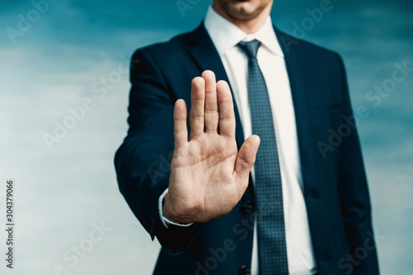 Fototapeta Businessman gesture. Male palm close-up in a gesture of stop. In the background a man in a blue suit with a tie.