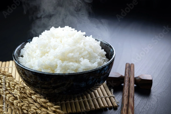Fototapeta Cooked jasmine rice in ceramic cups and chopsticks and Ear of rice Placed on a black wooden table. Close up shot. 45 degree angle.