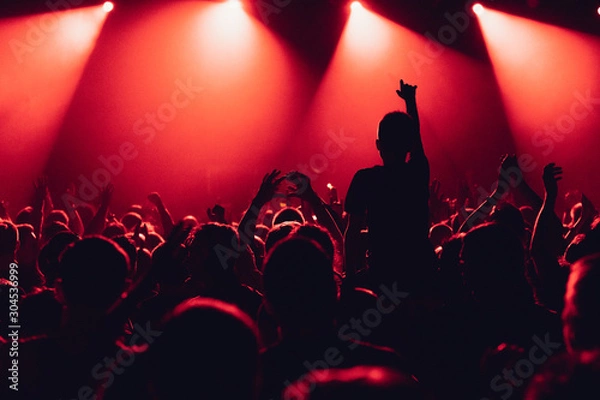 Fototapeta cheering crowd of unrecognized people at a rock music concert. crowd in front of bright stage lights. Concert audience at music concert. Smoke, concert spotlights.