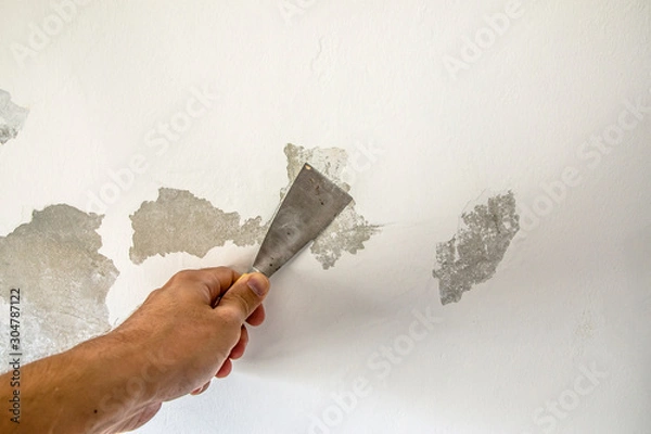 Fototapeta Work tool, putty knife in hand on a white wall background, work plasterer, cleaning the wall of old paint