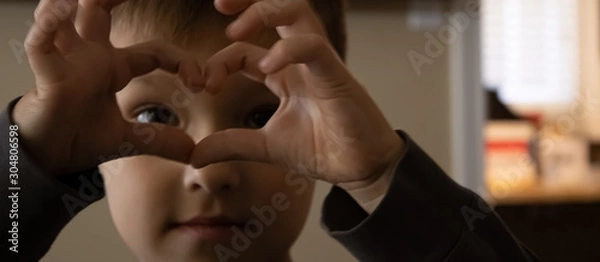Fototapeta Small baby boy holding his hands with the heart-shape figure and looking through it.close up
