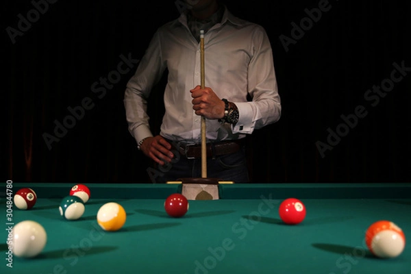 Fototapeta Sports game of billiards on a green cloth. Male player with a cue in his hands. Billiard balls with numbers on a pool table. Active leisure and entertainment. Billiards and billiard balls.