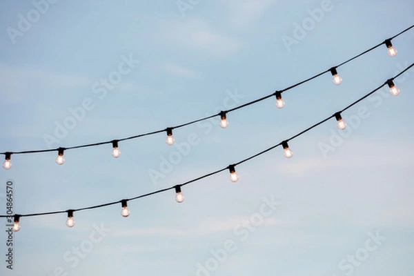 Fototapeta light bulbs garlands on a background of blue sky
