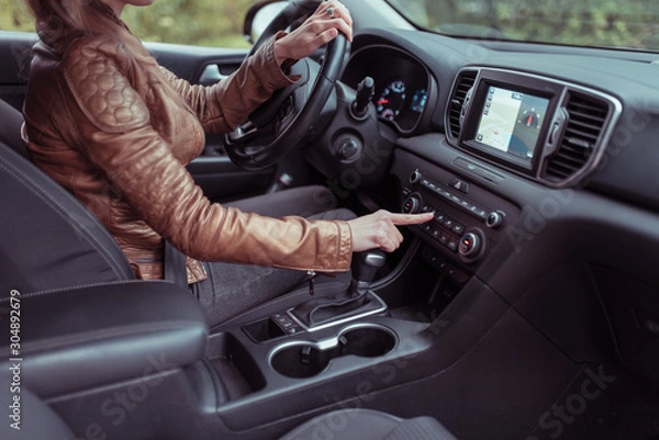 Fototapeta woman car interior includes button, application air conditioning selection, seat heating ventilation, automatic transmission, autumn spring forest park. Leather jacket. Screen with navigation.