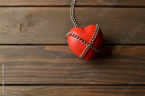 Fototapeta Heart and secured with the chain. Heart in chains on a dark wooden background. Red heart and secured with chains on a brown rustic table.