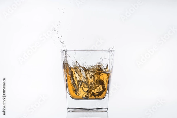 Fototapeta Alcohol drinks. Whiskey with ice. Rum with ice. Brown brandy with ice. Ice cube falling with splashes into a glass with alcohol