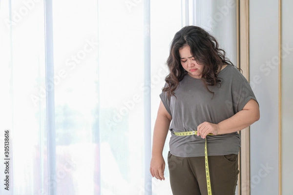 Fototapeta Asian fat women are sad because of the increase in size after checking with a tape measure.