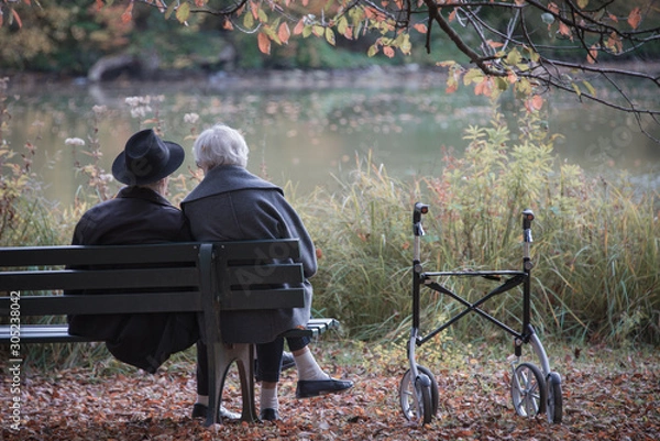 Fototapeta Senior couple man and woman are resting on a bench in the autumn park. Effect neutral and pastel color images.