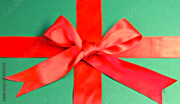 Obraz  red ribbon with a bow with a tail on a green background. gift wrap