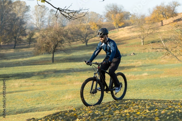 Fototapeta Cyclist in pants and fleece jacket on a modern carbon hardtail bike with an air suspension fork. The guy on the top of the hill rides a bike.
