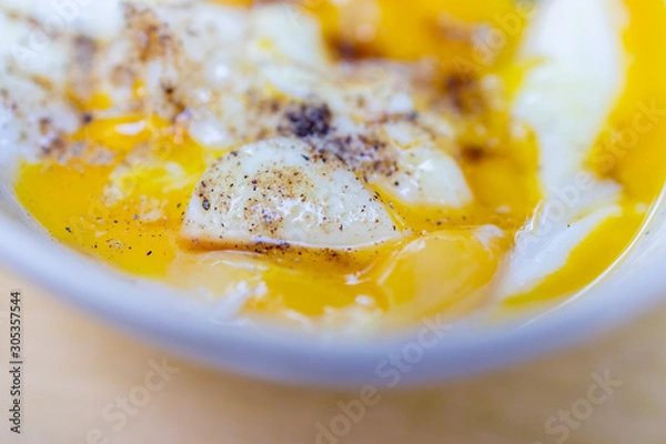 Fototapeta Soft boiled egg cracked open in a bowl with a hint of black pepper