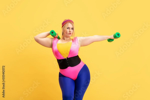 Obraz Young caucasian plus size female model's training on yellow background. Copyspace. Concept of sport, healthy lifestyle, body positive, fashion, style. Stylish woman practicing with green weights.