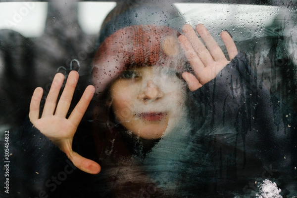 Fototapeta Beautiful toddler boy looking out car window outside. Drawing on window. Water drops and Frost patterns