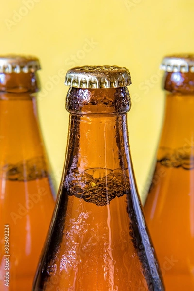 Fototapeta A chilled bottles with drink on yellow background. Beer in a dewy glass bottle closed with a lid.